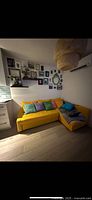 Yellow upholstered sectional couch against gallery wall with colorful pillows.