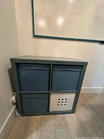 Front view of teal IKEA KALLAX shelf with four inserts in place; three teal fabric and one white plastic insert with cut-out squares.