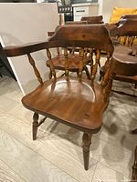 Photo showing one wooden captain's chair with curved seat, armrests, turned legs, and spindled backrest in solid pine with brown finish.