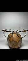 Front view of vintage Le Club Optique eyeglass frames with brass rims and tortoise shell arms displayed on a wooden stand.
