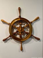 Front view of a circular wooden ship wheel wall decoration with eight wooden handles/spokes and a central hub, polished and made of varying wood tones.