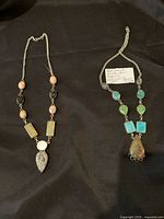 Two necklaces laid out showing the full length and pendants with varied gemstone beads
