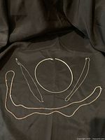 Four sterling silver chains laid out on black fabric showing various styles and lengths.