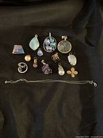 Photo of 13 assorted pendants and charms laid out on dark fabric with one silver tone chain