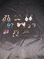 Top-down view of 9 pairs of assorted earrings laid on black fabric showing various designs and mixed metals.