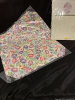 Photo showing four floral pattern placemats packaged in clear plastic and one packaged tablecloth.