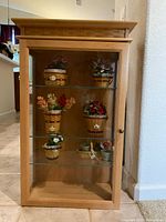 Front view of the Longaberger Collectors Club display cabinet showing wood frame and glass front door with shelves inside and collectible baskets.