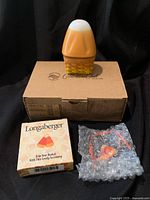 Miniature candy corn basket atop original Longaberger Collectors Club box, with accessory box and bubble wrapped candy corn toe-on accessory in front.
