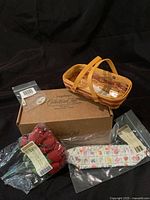 Photo showing miniature Longaberger basket, box labeled 'Collectors Club', artificial rose arrangement, fabric liner, and plastic protector in packaging