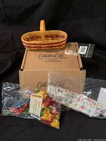 Miniature wooden basket on top of its original cardboard Longaberger Collectors Club box with packaged tie-on tag and floral fabric liner.