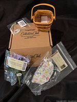 Photo showing miniature woven wood basket, plastic liner, floral insert, oval tie-on tag, and original box.