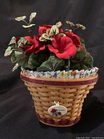 Front view showing the miniature Longaberger basket with the red geranium floral arrangement inside. The basket has the burgundy rim and base with the floral tie-on ornament visible.
