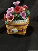Front view of the miniature Longaberger petunia basket with mini pink and purple petunia floral arrangement inside, showing the floral fabric liner and label.