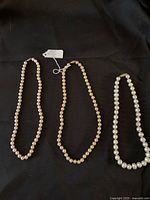 Three genuine pearl necklaces laid out on a black background, showing the overall length and the uniformity of pearl size and color for all three strands.