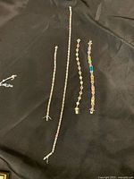Four pieces of costume jewelry laid out on a black fabric background: three bracelets and one necklace with multicolored rhinestones, varying stone shapes and sizes.