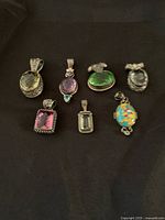 Top view of all 7 sterling silver gemstone pendants arranged on a dark surface, showing variety of colors and shapes.