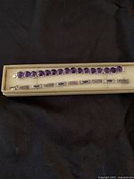 Pair of two sterling silver bracelets laid out in cream colored box on black background, showing front side with purple gemstones.