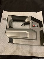 Side view of Porter Cable TS056 pneumatic staple gun showing the black and silver body, air connector, and trigger.