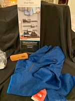 Photo showing blue North Face XL jacket, horse hair shoe brush with wooden handle, and boxed 4-tier white steel shoe rack.