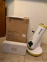 Photo of the Meade 114mm Dobsonian telescope and two boxes including the original shipping box with product details, placed on floor near a wall.