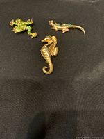 Set of three gold tone animal-shaped brooches including a seahorse, a lizard/gecko, and a frog.