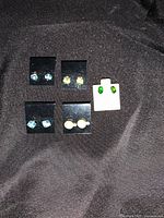 Photo of 5 pairs of stud earrings arranged on black and white earring cards showing blue, light blue, pearl, green gemstones.