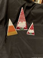 Three wooden triangular blocks with Christmas gnome designs facing forward on black background.