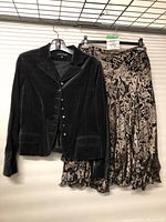 Full view of the Anne Klein black velvet jacket and patterned skirt hanging on rack