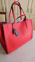 Red leather tote bag, front angle, showing shape and handles.