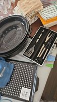 Photo showing roasting pans, BBQ cooking pan, hand towels, and apron with BBQ utensil set in a box