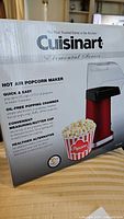 Photo of the popcorn maker's original box showing front panel with brand, product image, and features description.