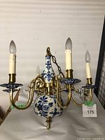 Front view of vintage Delft ceramic and brass chandelier showing four candle candle-style lights with white ceramic bobeches, brass arms and ceramic painted centerpiece.