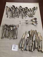 Wide view of flatware showing spoons, forks, knives, and serving utensils laid out on a white surface.