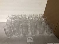 Overall view of all 28 glasses arranged showing 22 tall ribbed glasses and 6 short stemmed ribbed glasses.