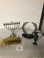 Three Judaica items: two menorahs and a small metal pitcher shown on neutral background.