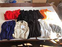 Nine folded knit cardigans displayed on a table showing the variety of colors and textures.