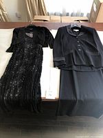 Full view of the black lace dress with matching shrug on the left and the black knit skirt and jacket suit on the right, both laid out flat.
