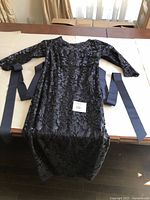 Full view of the gown laid flat, showcasing the black floral sequin pattern and long matching sash belt.