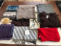 Full view of all scarves and wraps laid flat showing variety and colors including plaid, solid, and patterned scarves, some fringed edges