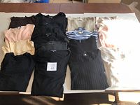 Collection of 12 knit sweaters and tops in various colors laid out on table, showing assorted styles and colors.