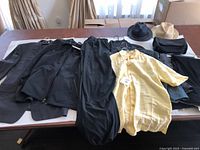Photo showing full lot of men's clothing items laid on table including suits, shirts, slacks, hats, and bag.