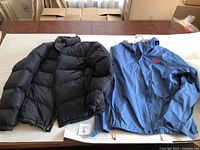 Two men's jackets laid flat on a table, a black Eddie Bauer puffer and a blue The North Face hooded jacket with red logo