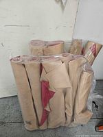 Seven rolled moving mats wrapped in clear plastic, beige with red backs, arranged upright showing widths and rolled ends.
