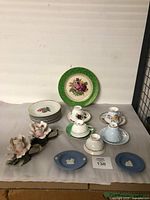 Display of all ceramic teacups, plates, and two ceramic flower candle holders on a cloth-covered surface.