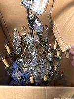 Photo showing the overall vintage brass chandelier inside a cardboard box, with candle-style light holders and glass crystals visible.