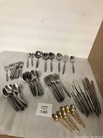 Full set of vintage flatware laid out on white cloth showing forks, knives, spoons, and gold-tone spoons.