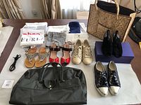 Overview of all items on table: five pairs of women's shoes, two handbags, multiple dust bags and cloth bags for shoes and brand protection.
