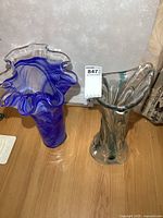 Two large art glass vases side by side on floor, showing colors and shapes including ruffled rims
