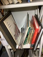 Shelf view of a mix of books including a large-format vintage book and several smaller books.