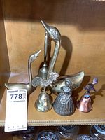 View of brass swans and various decorative bells with figures including rooster and lady in dress.